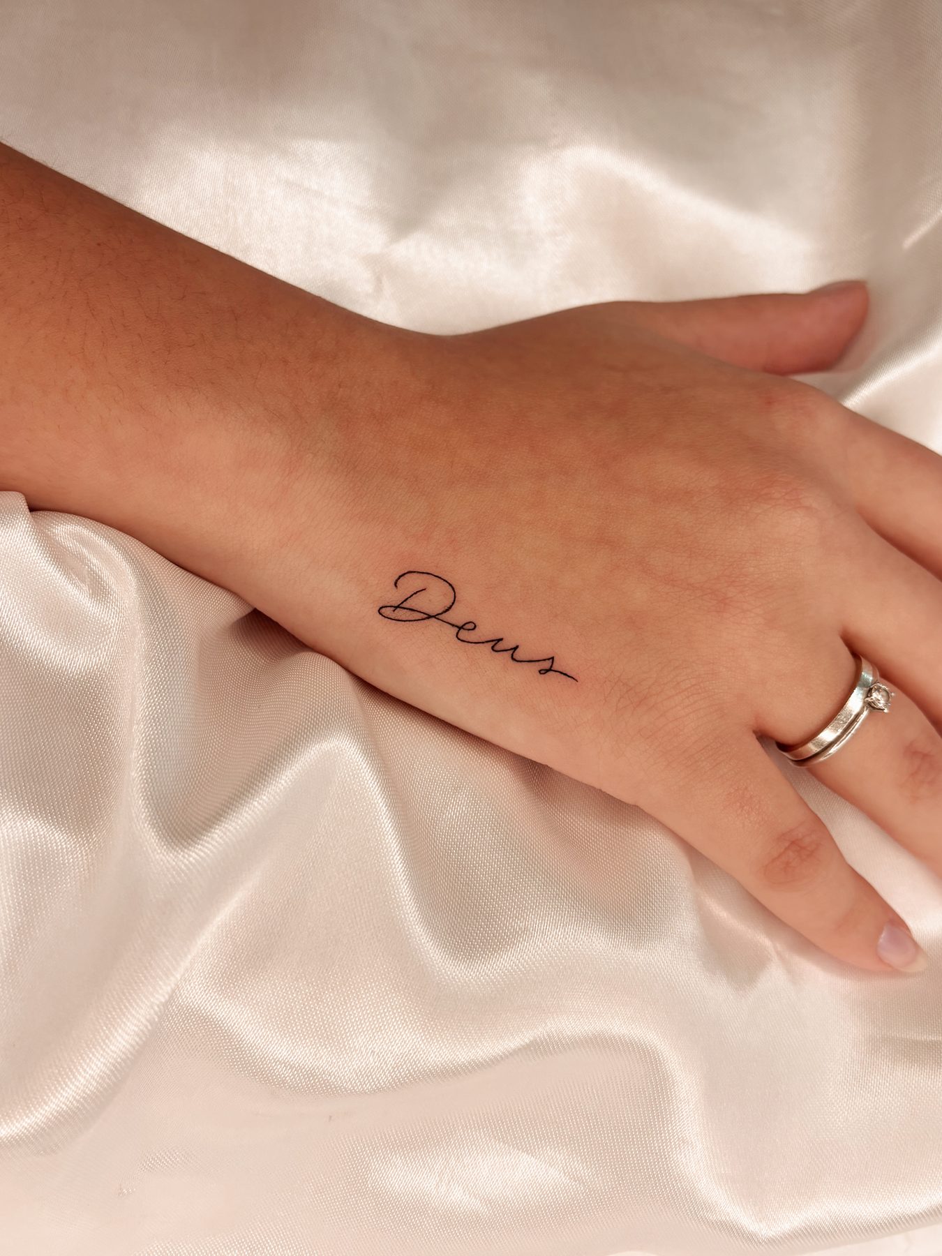 Tatuagem fineline de caligrafia 'Deus' na mão