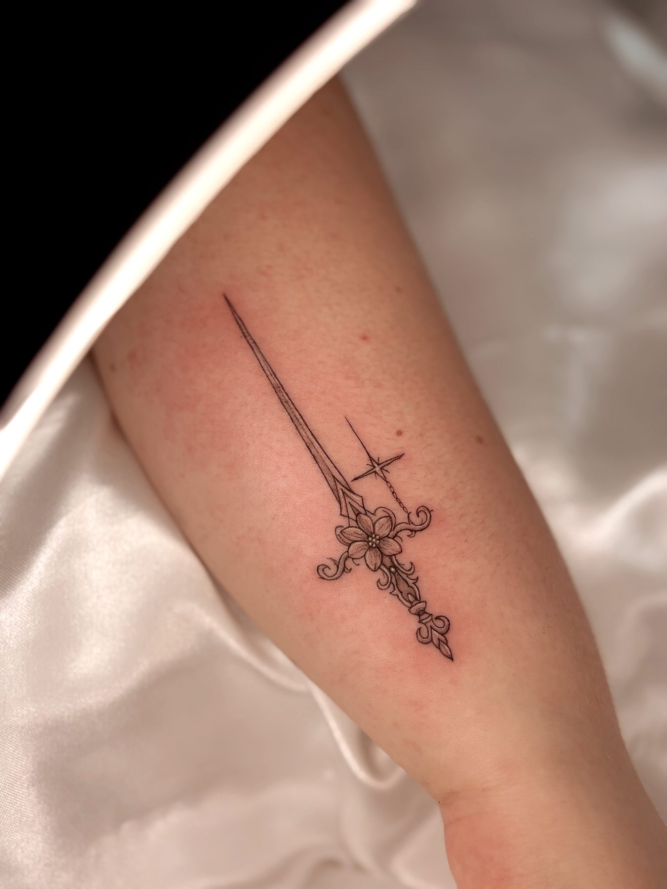 Tatuagem fineline de espada e flor no antebraço