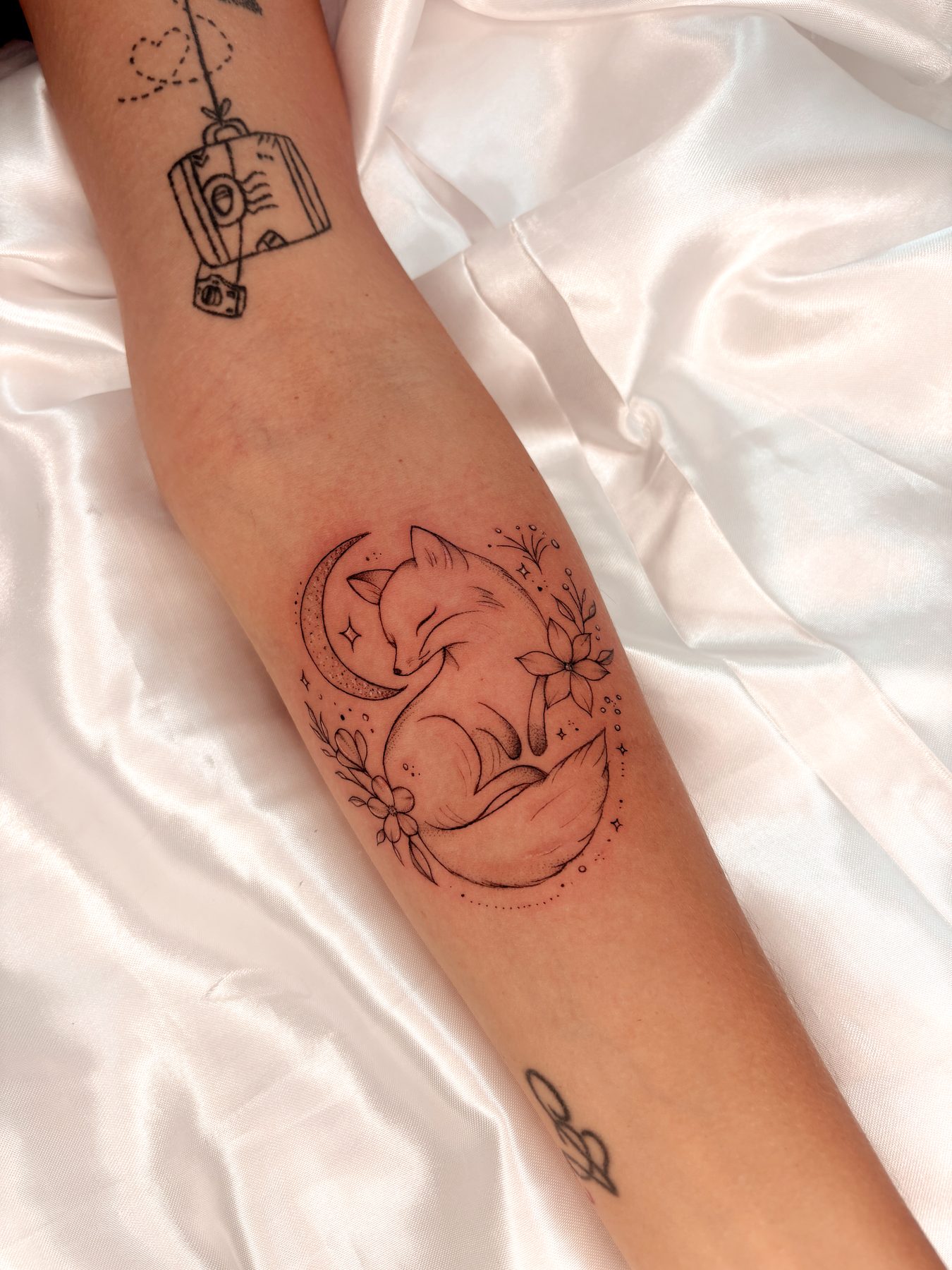 Tatuagem fineline de raposa dormindo entre luas
